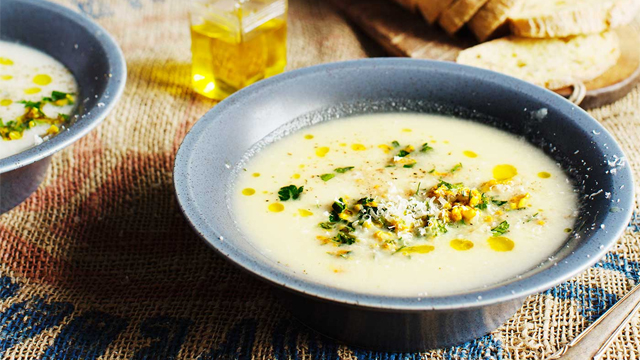 Blomkålssoppa i en skål, på ett matbord med bröd bakom.