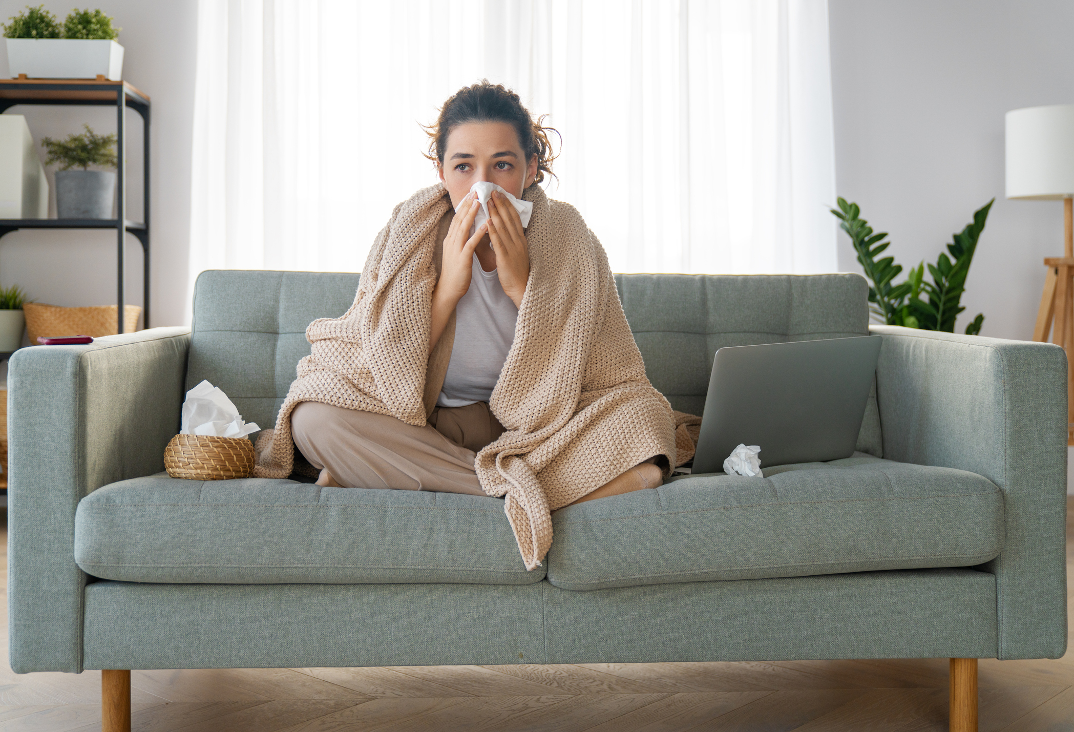 Sick woman sitting on couch, wrapped in a blanket