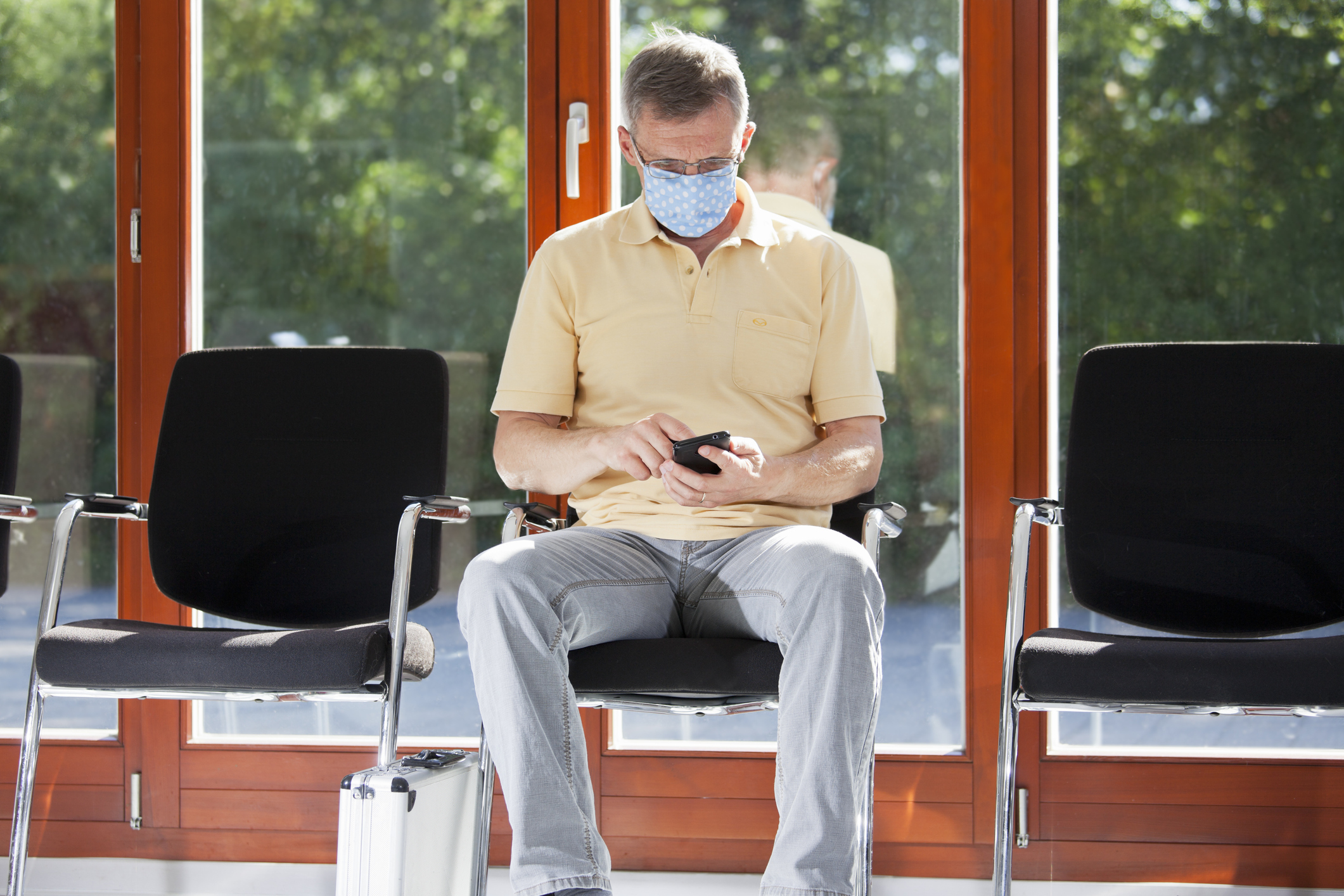Man sitting, wearing a mask, looking at his phone