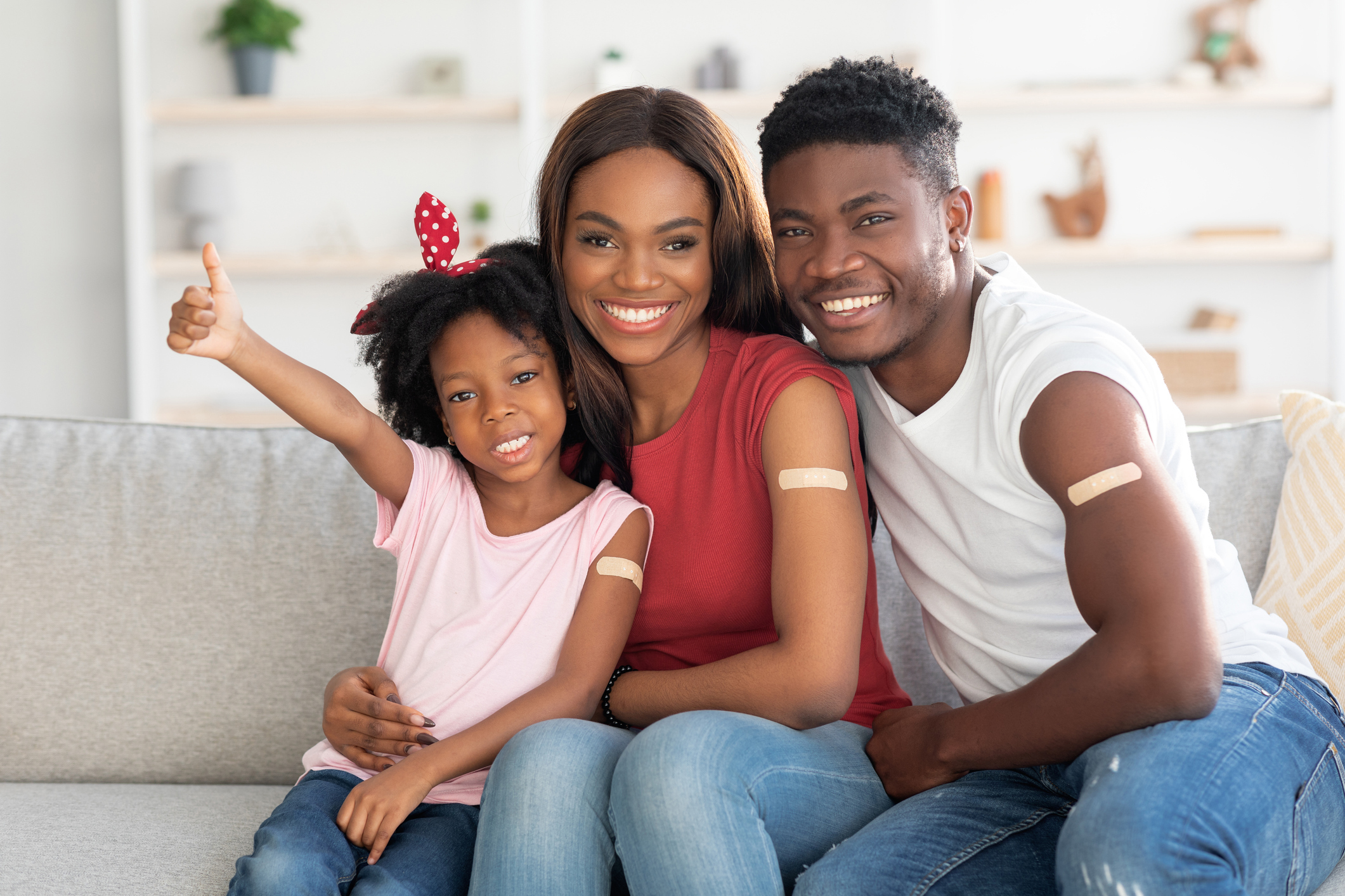 Familia de 3, mamá, papá e hija, cada uno con tiritas en el brazo que indican que se vacunaron recientemente.