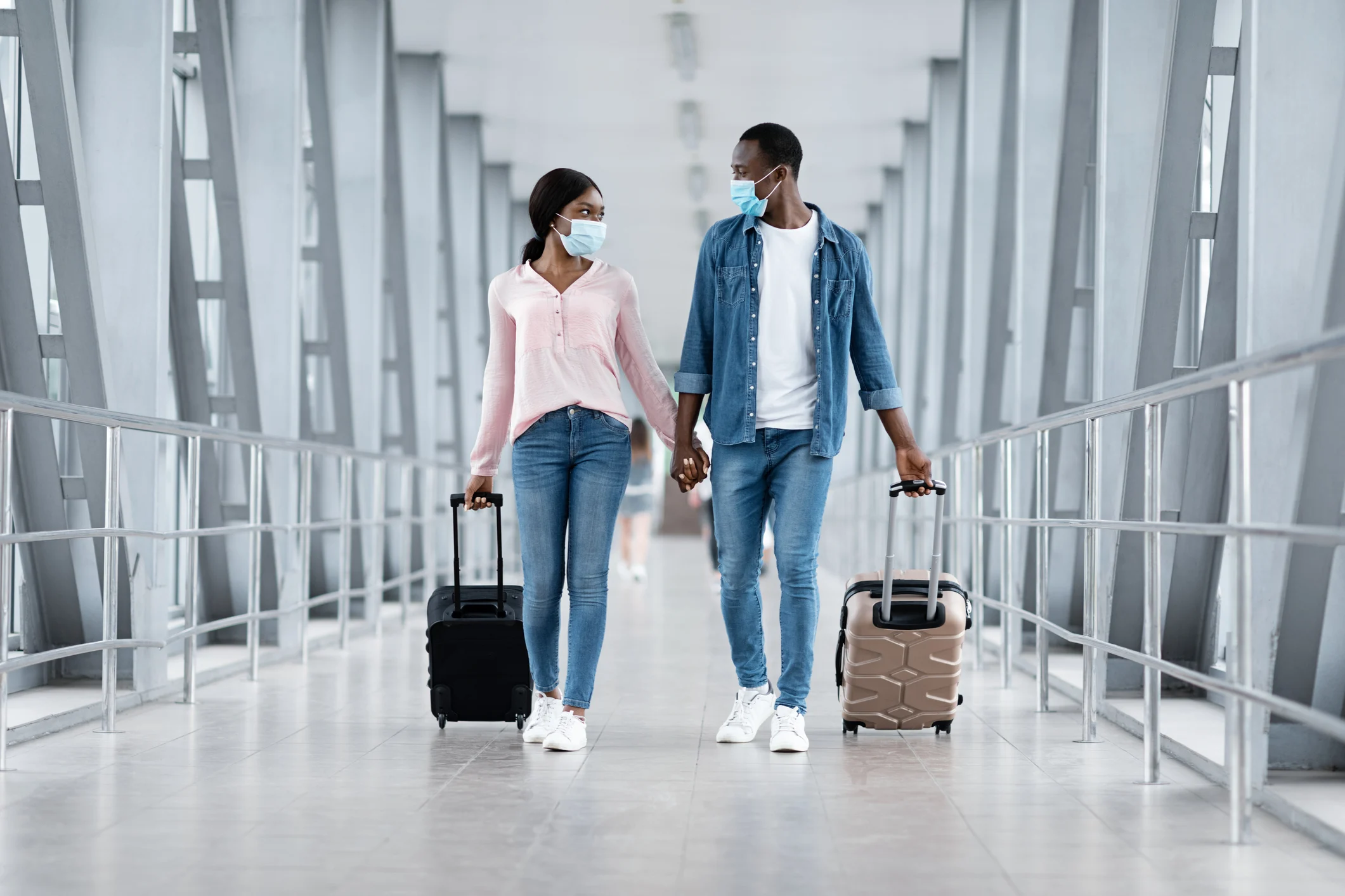 Couple holding hands, wearing masks, in airport