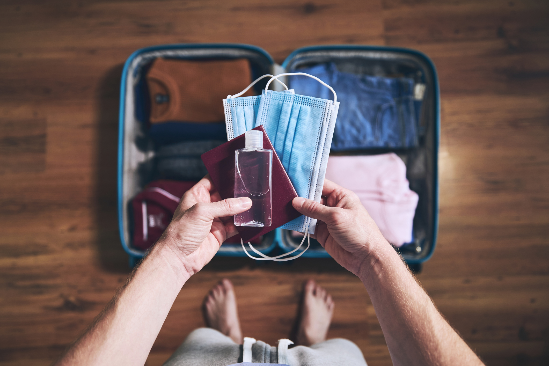 Suitcase packed for travel, person holding masks