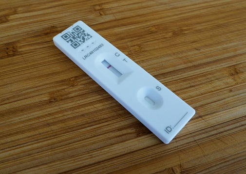 A COVID antigen test cassette sitting on a table. The control line shows the test has been used, and no test line shows the test reuslt is negative.