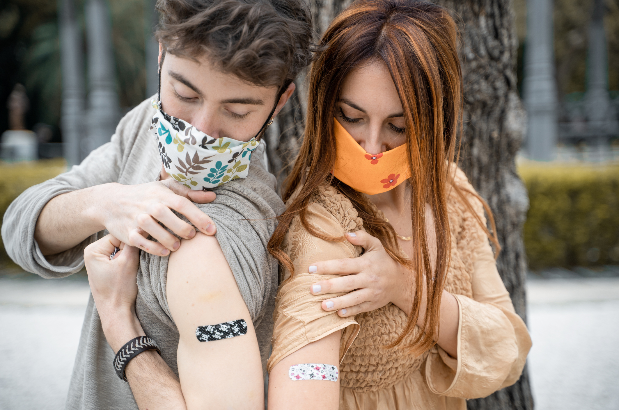 Two people standing back to back, wearing masks and showing their vaccinated arms