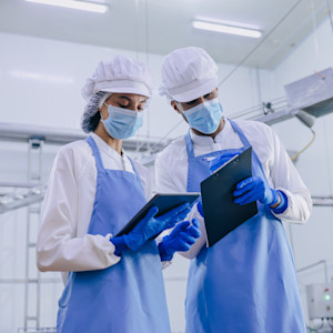 Two food hygiene officer inspecting and certifying the cleanliness of a food production facility while carrying clipboards.