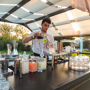 A bartender pours a cocktail at an outdoor bar at an event.