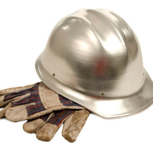 A metal hard hat rests on top of worn work gloves, representing basic personal protective equipment for industrial or construction work.