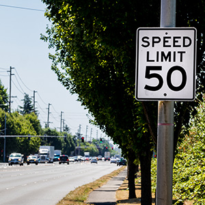 A speed limit sign on the right side of the road near a tree.