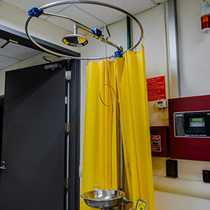 An indoor emergency eyewash and safety shower station is installed inside an industrial workspace, with a bright yellow privacy curtain.
