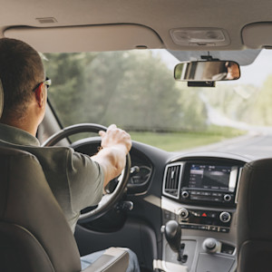 An interior view of a man driving an SUV on a two-lane country road.