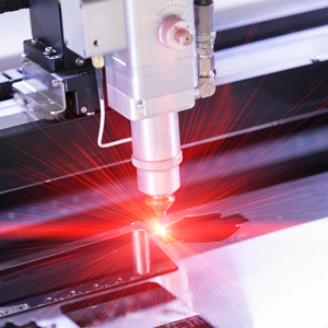 A close-up view of an industrial laser cutting machine using a bright red laser to cut a metal sheet in a manufacturing setting.