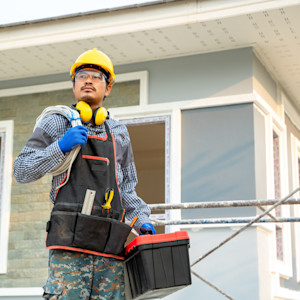 A male construction worker stands next to a new home under construction.
