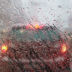 Car seen through a rain-covered windshield with brake lights glowing.