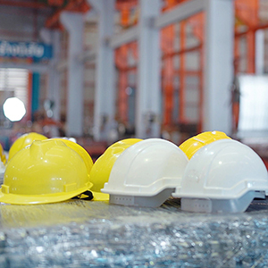 Several yellow and white construction hard hats sit on a table in an industrial worksite, with equipment and structural framing in the background.