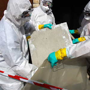 A team of workers in white disposable protective suits, goggles, respirators and gloves is performing asbestos abatement. 