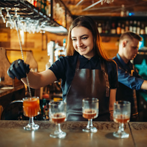 A smiling female bartender mixes drinks behind a bar.