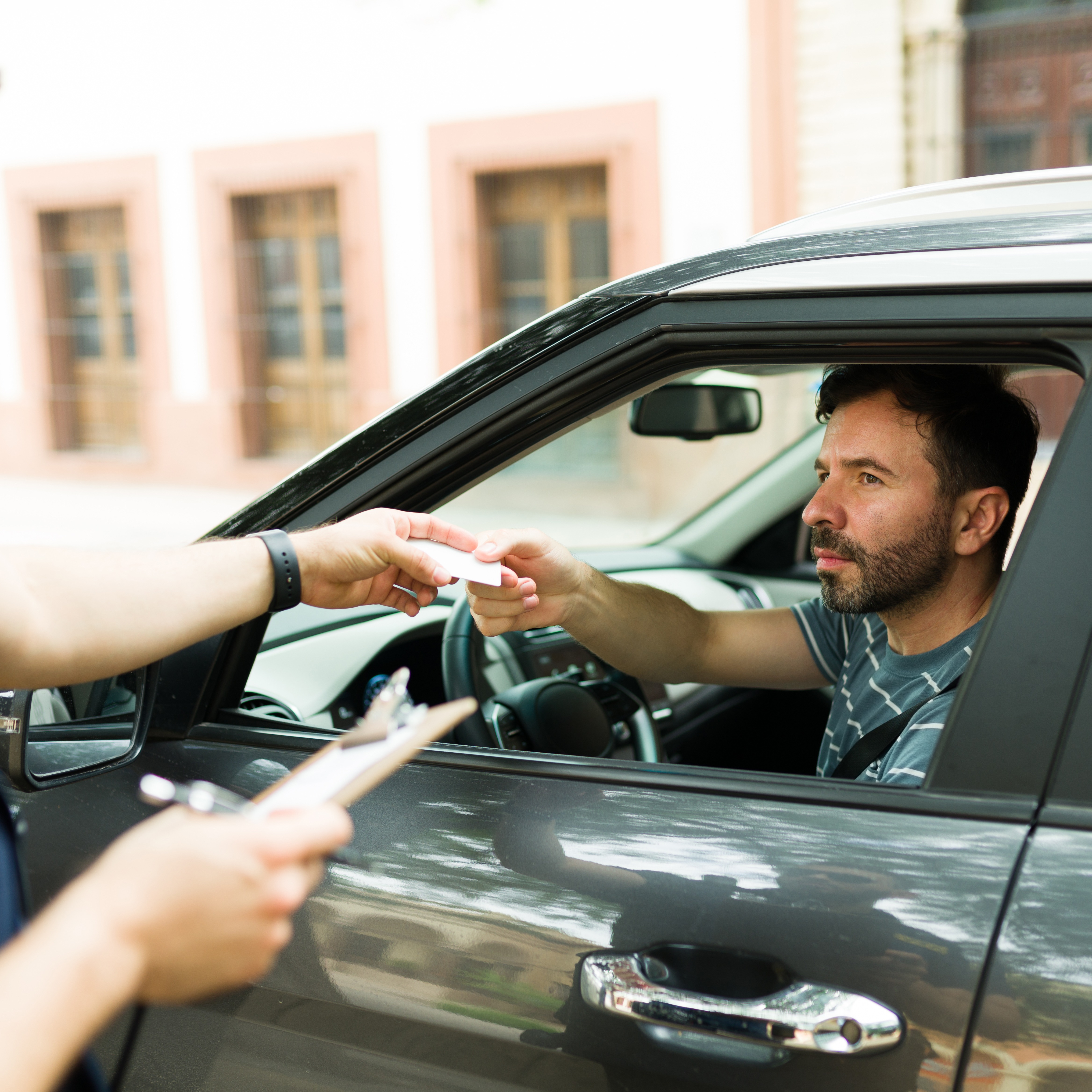 Police officer writing a speeding ticket to a male driver in a gray SUV.
