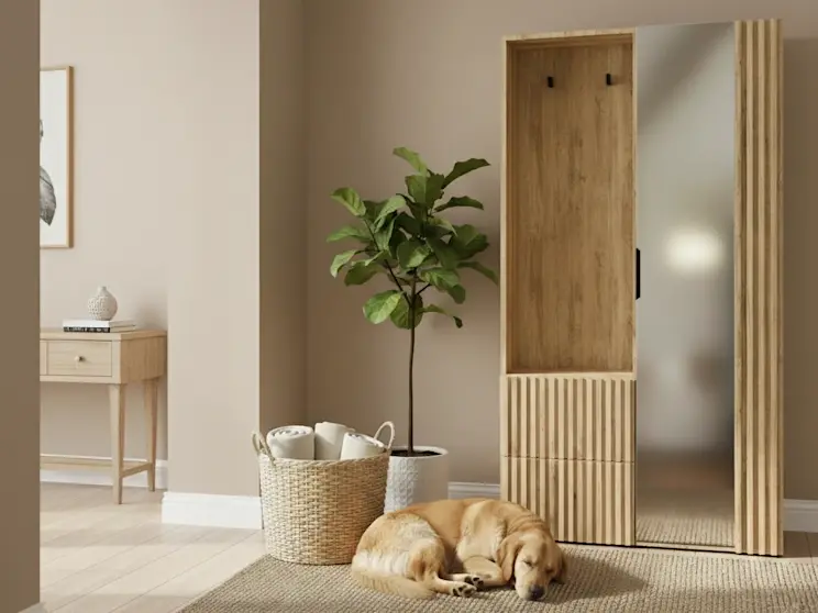 Przedpokój urządzony w ciepłych barwach z garderobą Vimerio z lustrem i lamelami oraz praktycznym panelem na kurtki. W kadrze widać kosz, roślinę i dywan, które ocieplają wnętrze i ułatwiają utrzymanie porządku na co dzień.