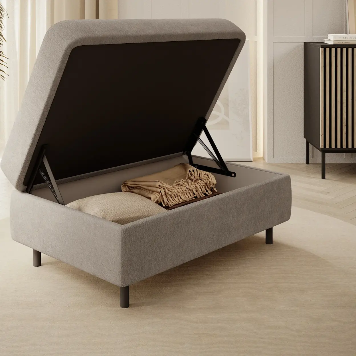 Nowoczesna pufa Gomsi Touch 18 z funkcją schowka – podnoszone wieko na czarnych siłownikach ułatwia odkładanie koców i poduszek. Pufa stoi na dywanie w jasnym salonie, obok komody Meorati i rośliny w donicy przy zasłonach.