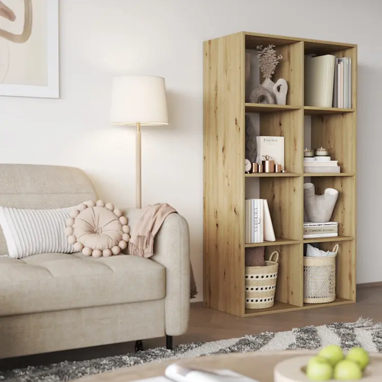 Regał Postto w ciepłym odcieniu drewna ustawiony obok jasnego narożnika Gomsi w tkaninie Manhattan 18. Przytulny salon z lampą stojącą, poduszkami i dekoracjami na półkach.