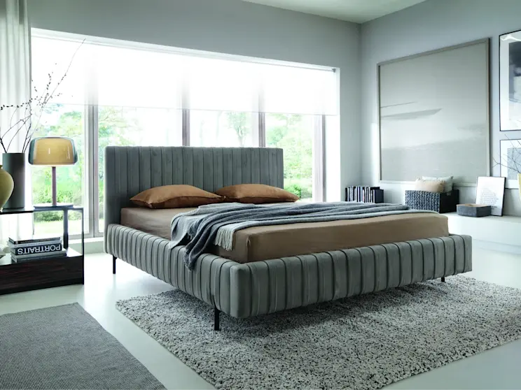 Nowoczesne łóżko Plissa z miękkim zagłówkiem i tapicerowaną ramą, tworzące komfortową i spokojną przestrzeń do snu.