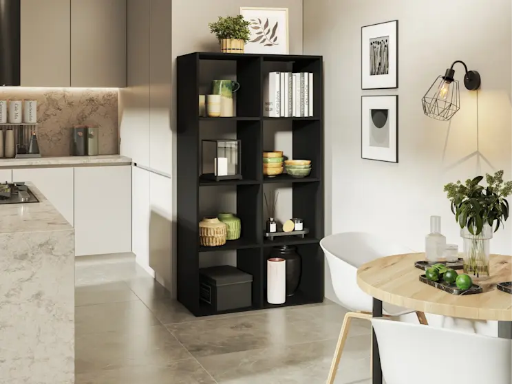 Regał Postto w kolorze czarnym ustawiony przy jasnej ścianie, wypełniony książkami, miskami i ozdobami. W tle minimalistyczna kuchnia i stół z jasnym blatem, a klimat wnętrza podkreśla kinkiet Bendinni.