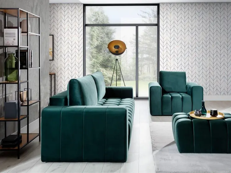 Komplet wypoczynkowy Lazaro Monolith 37 w odcieniu butelkowej zieleni ustawiony w jasnym salonie z dużym oknem. Sofa i fotel mają miękką tapicerkę oraz pikowane siedziska, a obok stoi pufa z tacą i dodatkami.