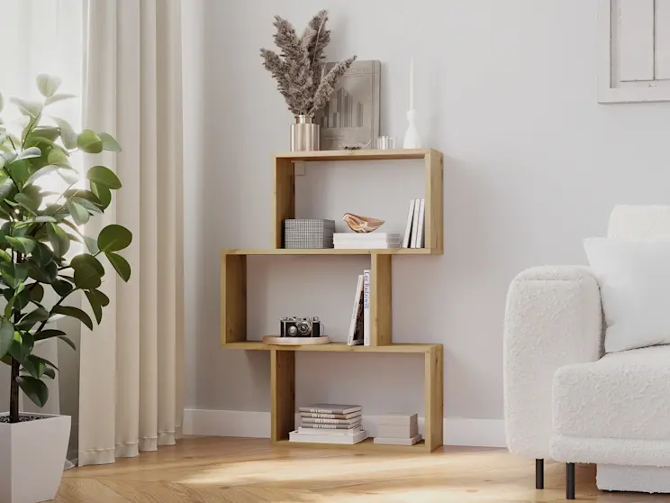 Jasny salon z regałem Evertti w dekorze drewna i kanapą Dalia Royal 01, obok rośliny w donicy i beżowych zasłon.