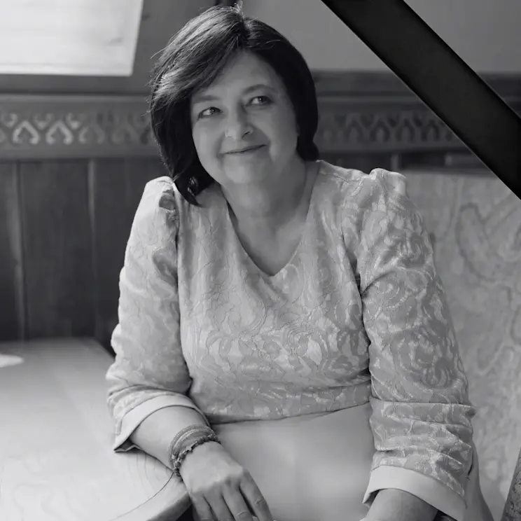 Portret Renaty Dworak w czarno-białej tonacji, siedzącej przy stole. Na zdjęciu widoczna jest czarna wstążka żałobna w prawym górnym rogu, symbolizująca pamięć po zmarłej. Renata Dworak spogląda z delikatnym uśmiechem w bok, ubrana w elegancką koronkową sukienkę.