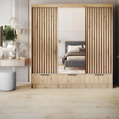 Inspirowana dębem artisan szafa z przesuwanymi frontami z lamelami i lustrem, ustawiona w jasnej sypialni z elegancką toaletką i rośliną.