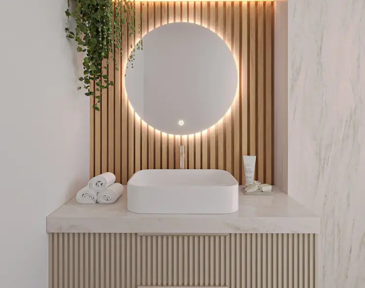 Okrągłe lustro Orandiu LED z podświetleniem zamontowane nad białą umywalką nablatową w jasnej łazience. Tło tworzą drewniane lamele, obok leżą zwinięte ręczniki i kosmetyki, a całość wygląda ciepło i nowocześnie.