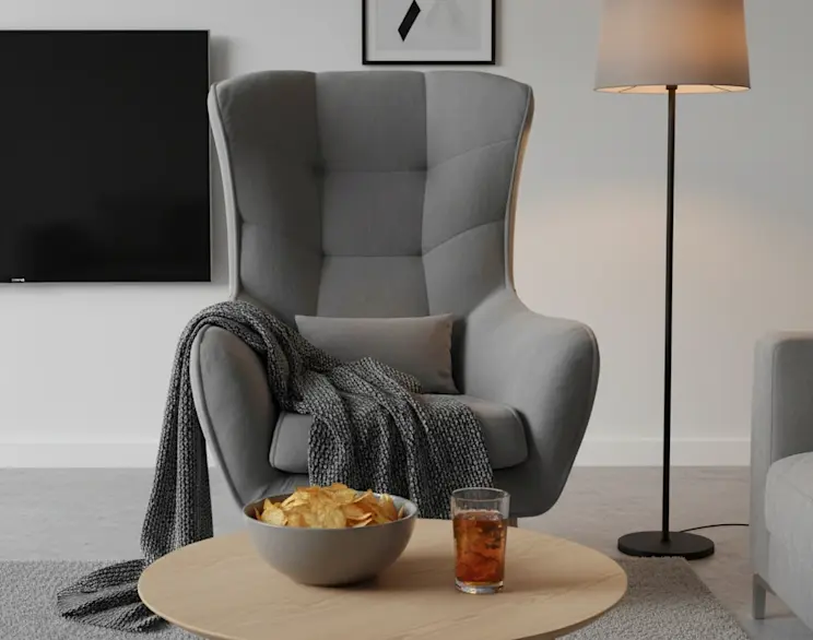 Szary fotel uszak Arti w tkaninie Monolith 84 z wysokim oparciem i wygodnymi podłokietnikami. W aranżacji salonu widać pled, poduszkę, stolik kawowy z przekąskami oraz lampę stojącą, tworząc przytulny klimat.