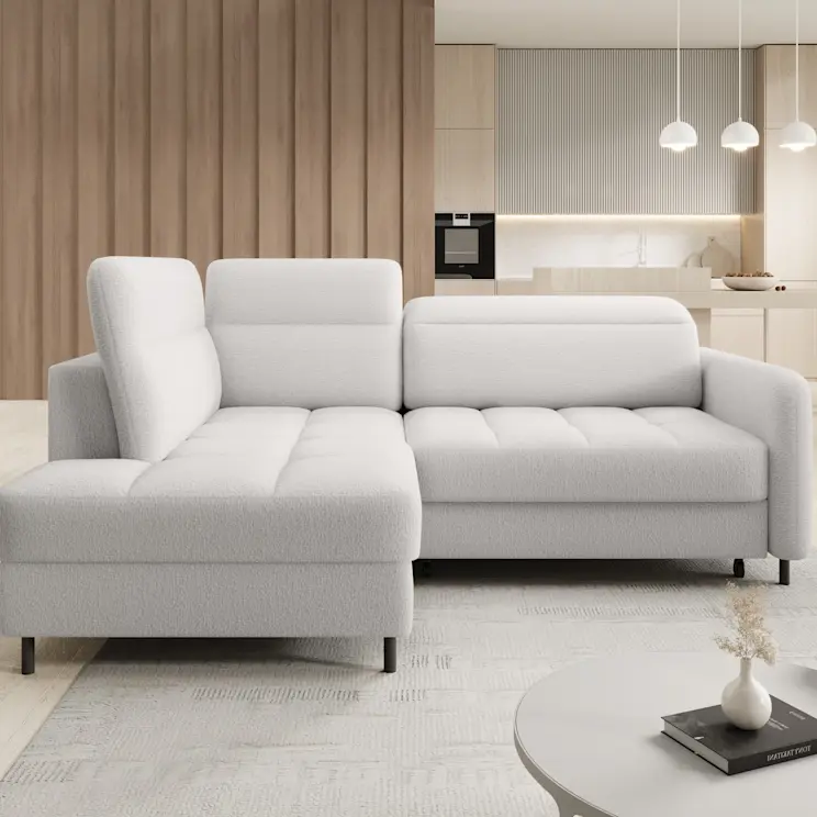 Jasny narożnik Barea w tkaninie Royal 01 ustawiony w nowoczesnym salonie połączonym z kuchnią. Miękkie siedziska i szerokie oparcia tworzą wygodne miejsce do odpoczynku, a wnętrze ocieplają drewniane lamele w tle.