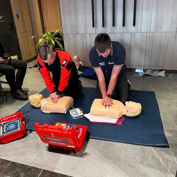 Szkolenie z pierwszej pomocy w ELTAP: uczestnicy ćwiczą resuscytację krążeniowo-oddechową na fantomach na macie. W kadrze widać sprzęt AED oraz czerwone walizki ratownicze, co podkreśla praktyczny charakter treningu.