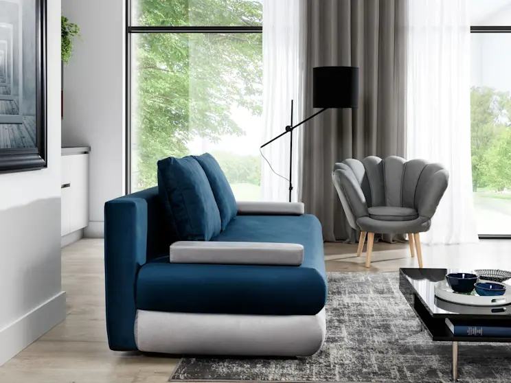 Kanapa Milo w tkaninie Monolith 77/Monolith 84 w kolorze granatowo-szarym, pokazana z boku w jasnym salonie. W tle duże okna z zasłonami, czarna lampa stojąca, szary fotel i dywan w odcieniach grafitu.