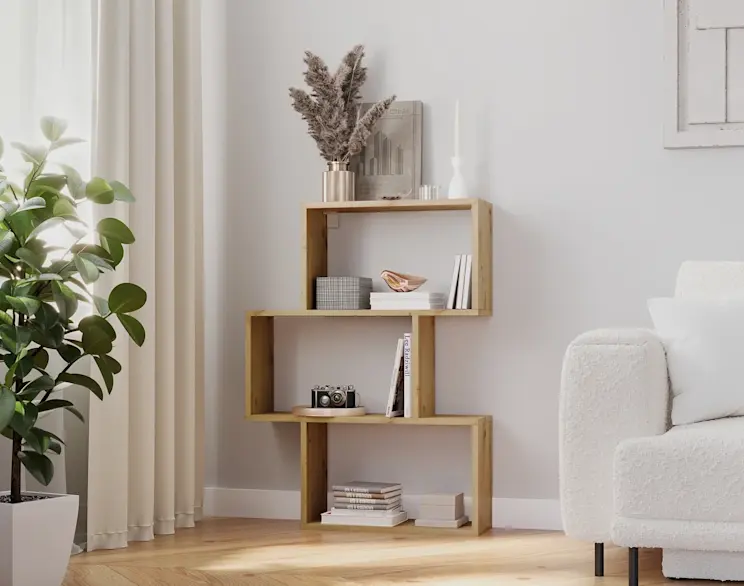 Regał Evertti w dekorze drewna z asymetrycznymi półkami, ustawiony w jasnym salonie obok rośliny i beżowych zasłon.