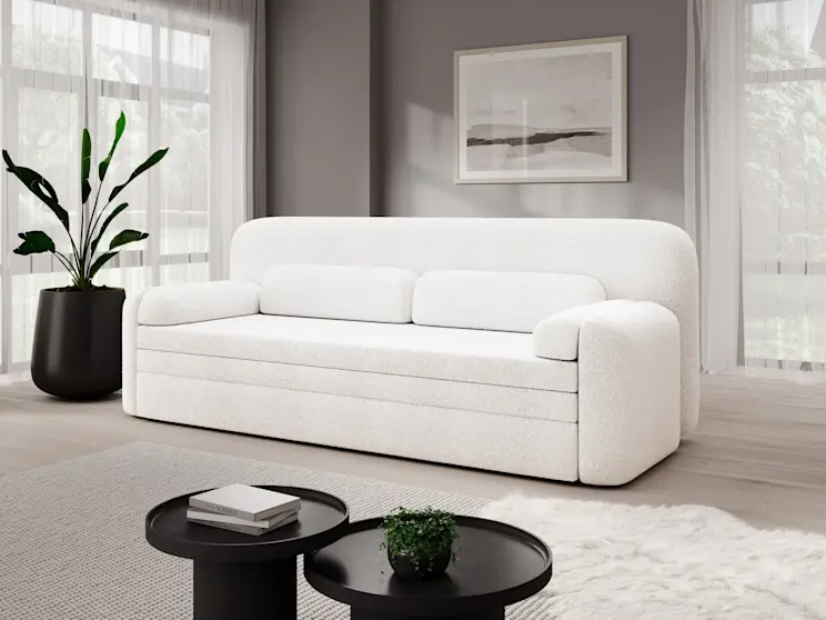 Nowoczesna aranżacja salonu z kanapą Elioss Royal 01 w białej tkaninie boucle. Kanapa o obłych kształtach stoi na tle szarej ściany z obrazem, obok dużego okna z lekkimi zasłonami. 