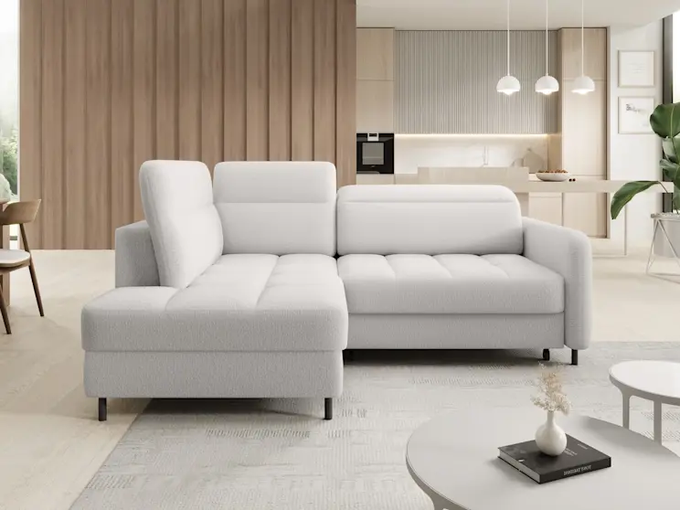 Jasny narożnik Barea w tkaninie Royal 01 ustawiony w nowoczesnym salonie połączonym z kuchnią. Miękkie siedziska i szerokie oparcia tworzą wygodne miejsce do odpoczynku, a wnętrze ocieplają drewniane lamele w tle.