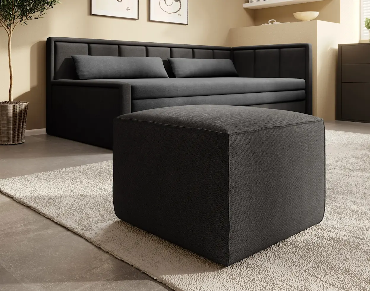 Sofa dwuosobowa rozkładana Fulgeo w ciemnoszarej tapicerce, pokazana w przytulnej aranżacji salonu. Przed sofą stoi duża, kwadratowa pufa, a całość dopełnia jasny dywan, roślina w donicy i dekoracje na ścianie.