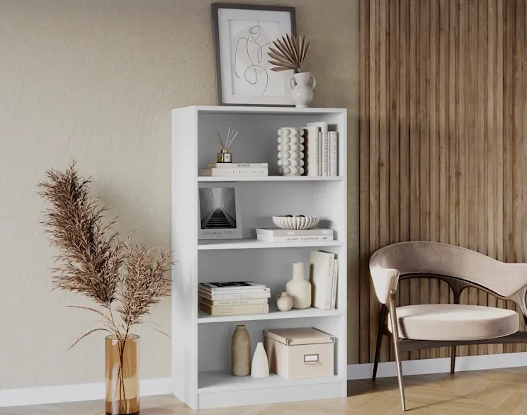 Biały regał Pocett z otwartymi półkami w przytulnej aranżacji salonu. Na półkach książki, ceramika i dekoracje, a obok widać fotel w jasnej tapicerce i drewniane lamele na ścianie.