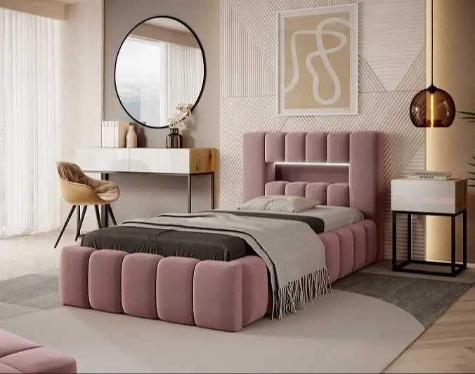 Różowe łóżko tapicerowane Lamica 90x200 cm w tkaninie Nube 24 z praktycznym pojemnikiem na pościel. Przytulna aranżacja sypialni z jasnym dywanem, lampą wiszącą i toaletką z okrągłym lustrem.