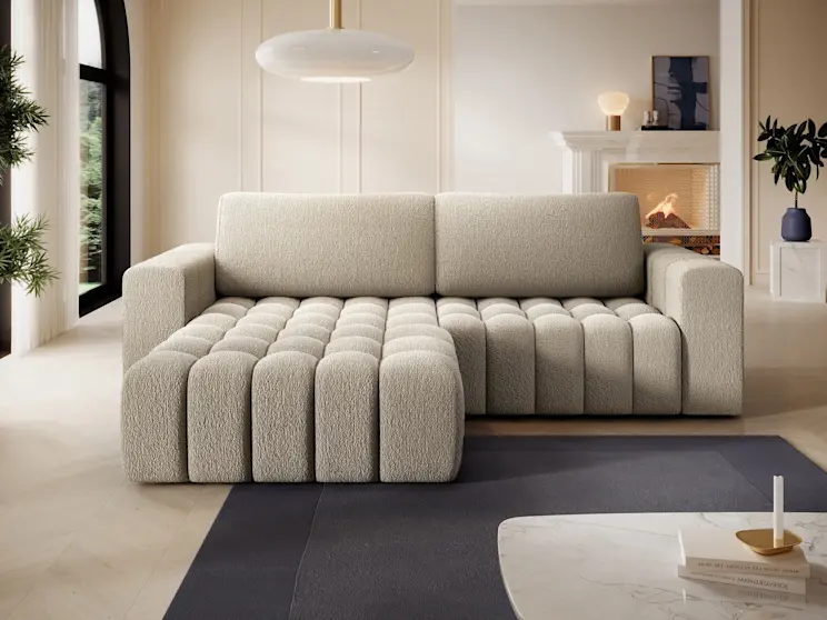 Beżowy narożnik Bonett Royal 20 w eleganckiej aranżacji wnętrza z kominkiem i dużą lampą sufitową. Głębokie siedzisko z regularnym pikowaniem oraz szerokie podłokietniki podkreślają komfort codziennego relaksu.