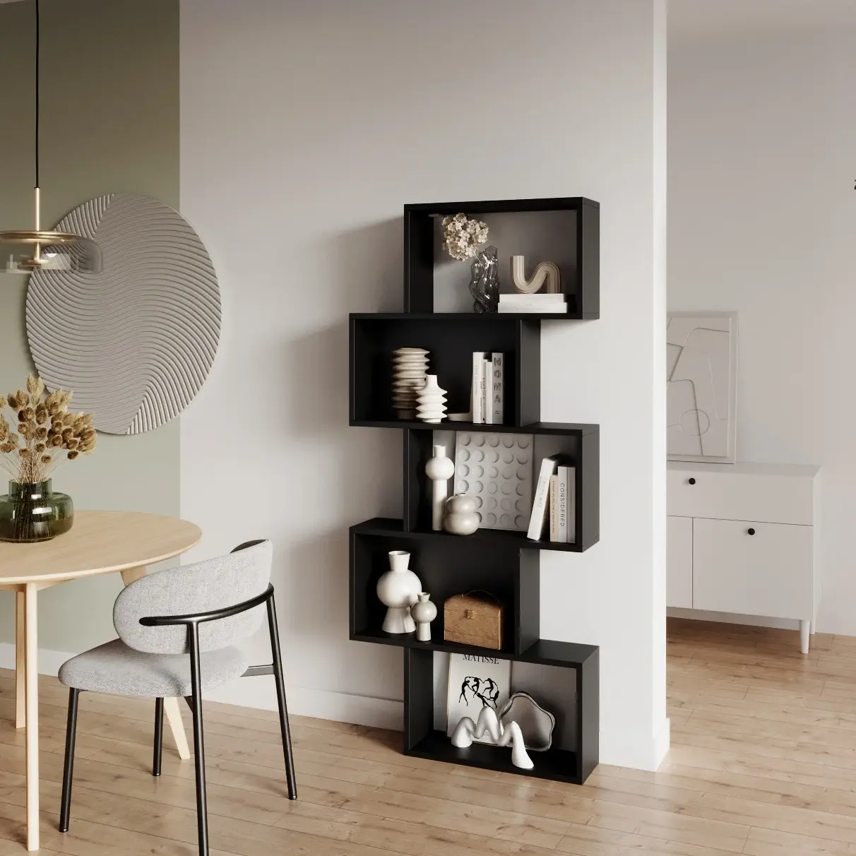Czarny regał Sottis o geometrycznej, przesuniętej formie ustawiony przy ścianie w nowoczesnym wnętrzu. Na półkach stoją książki i dekoracje, a obok widać stół i krzesło w strefie jadalni.