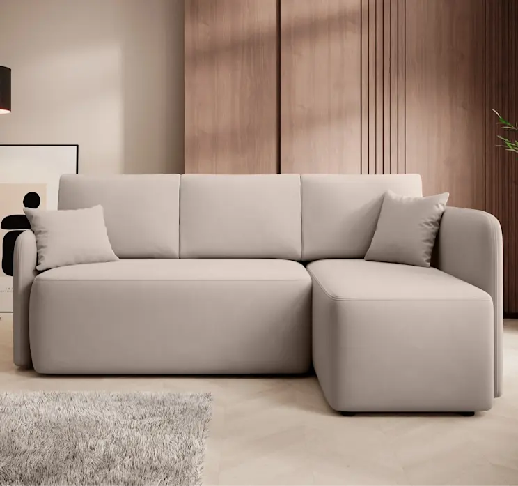 Beżowy narożnik Hadson Sola 18 z poduszkami na siedzisku stoi na jasnej podłodze z dywanem. Mebel znajduje się w eleganckim pomieszczeniu z drewnianą ścianą i dekoracyjnym obrazem za lampą.