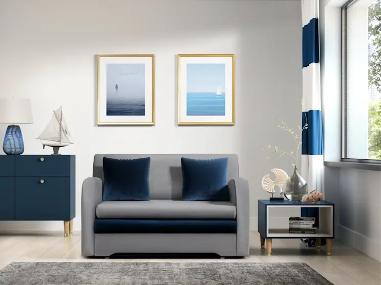 Szara kanapa Ario z granatowymi poduszkami zestawiona z dywanem Codrila w jasnym salonie w nadmorskim stylu, z dekoracjami w odcieniach granatu.
