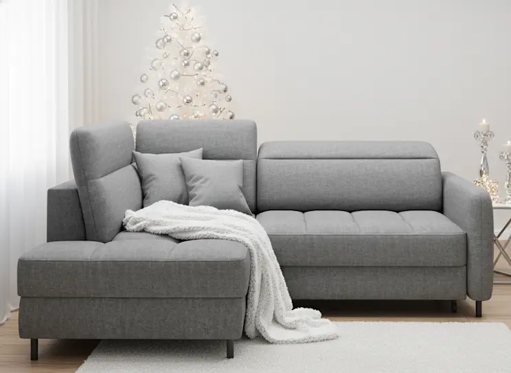 Szary narożnik w nowoczesnym salonie z białą choinką i srebrnymi ozdobami, tworzący elegancką, świąteczną atmosferę pełną ciepła.