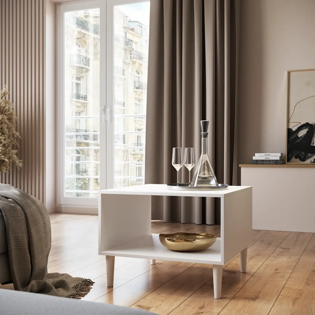 Biały stolik kawowy Dullum w nowoczesnym salonie z drewnianą podłogą. Prosta forma, dolna półka i eleganckie dodatki na blacie.