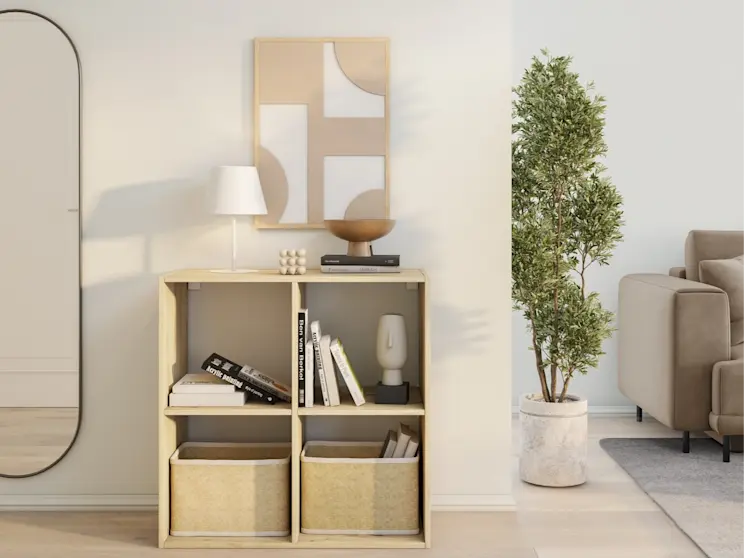 Jasny regał Jugis do salonu lub przedpokoju, z czterema otwartymi przegrodami i miejscem na kosze. Aranżacja w stylu skandynawskim z obrazem nad meblem i rośliną w donicy podkreśla przytulny charakter wnętrza.