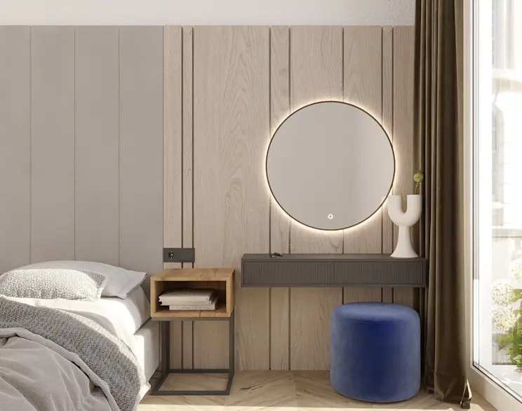 Okrągłe lustro LED Divissi z delikatnym podświetleniem nad grafitową toaletką w sypialni. Obok granatowa pufa Linsy, drewniane panele na ścianie i duże okno z ciemnymi zasłonami, tworzące przytulną strefę do makijażu.