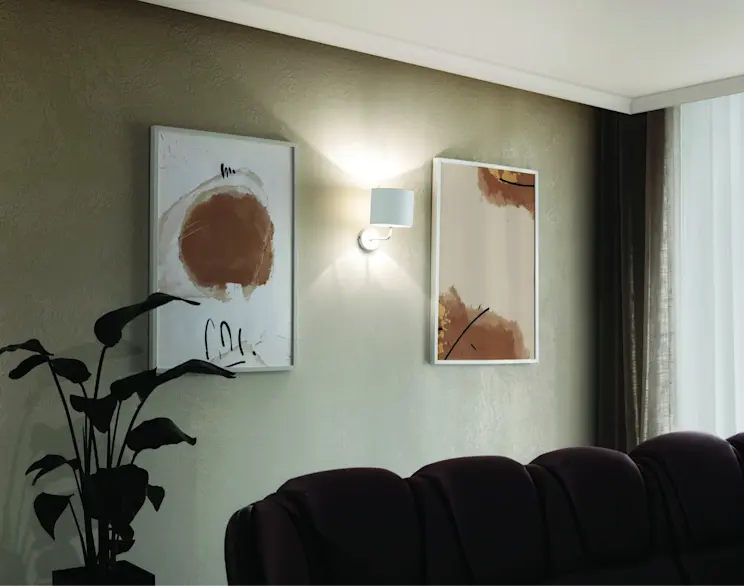 Biały kinkiet Vespillo zamontowany na ścianie w salonie, oświetlający dwa abstrakcyjne obrazy i tworzący nastrojową, elegancką atmosferę.